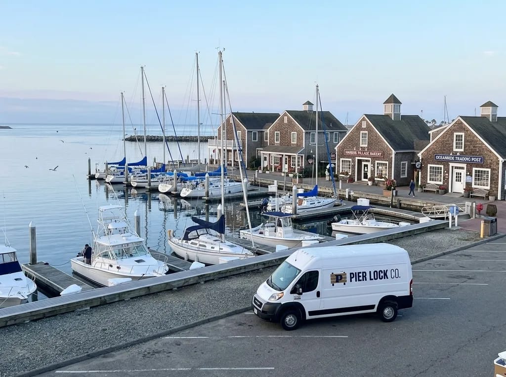 Pier Lock Co. van parked at Oceanside Harbor with boat slips and Harbor Village shops